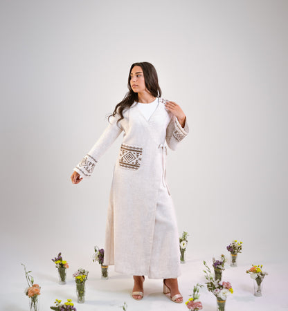 Woman in a beige linen kimono abaya with floral decorations on a light gray background