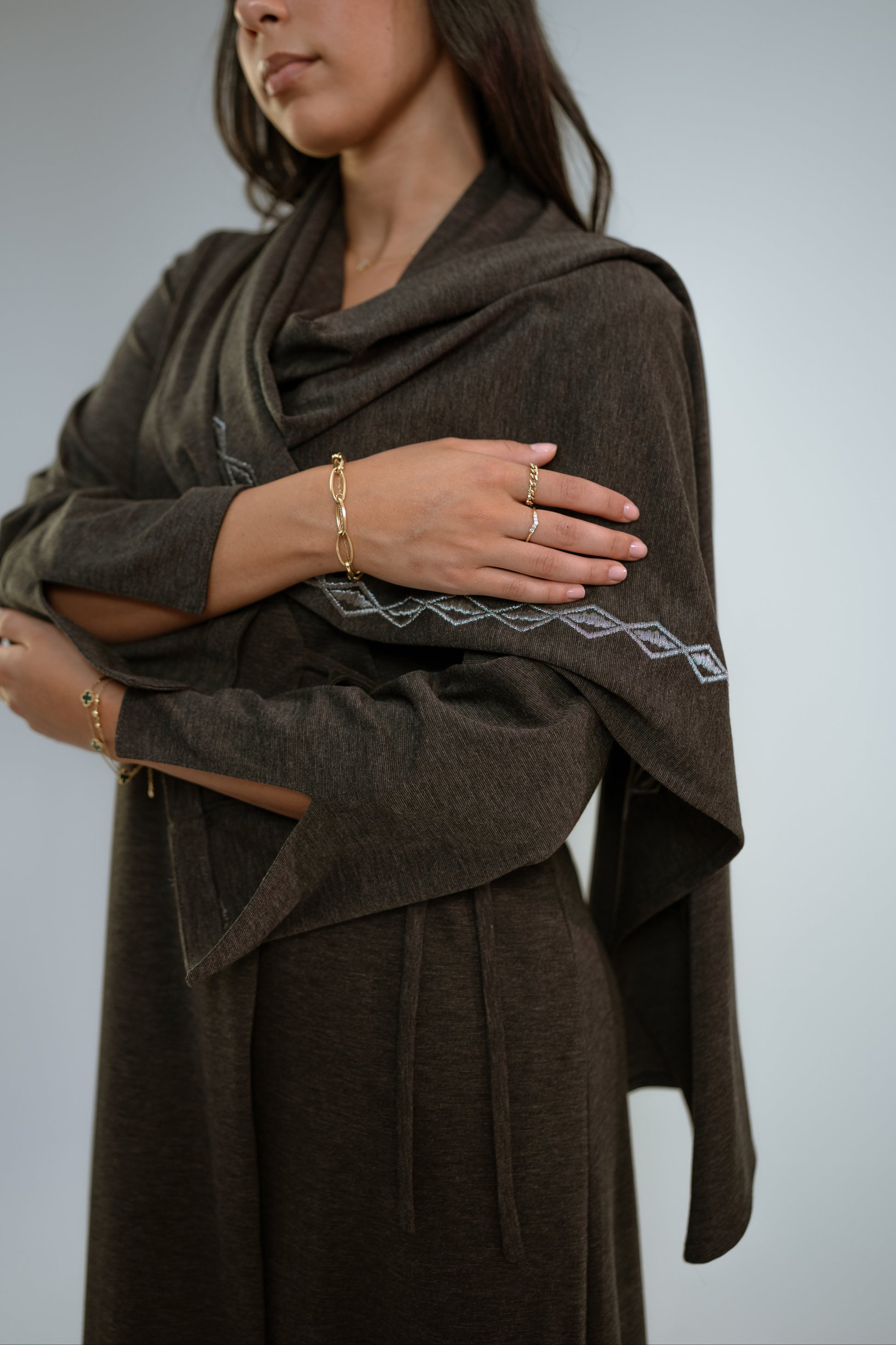 Woman wearing a dark gray abaya with n embroidered shawl standing in front of a light background